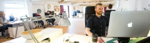 man on computer in an office with other people