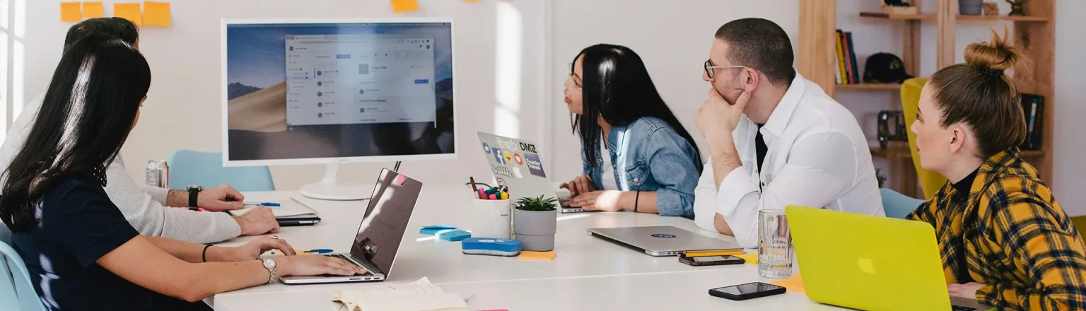 A mix of people around a table reviewing what is on a computer screen