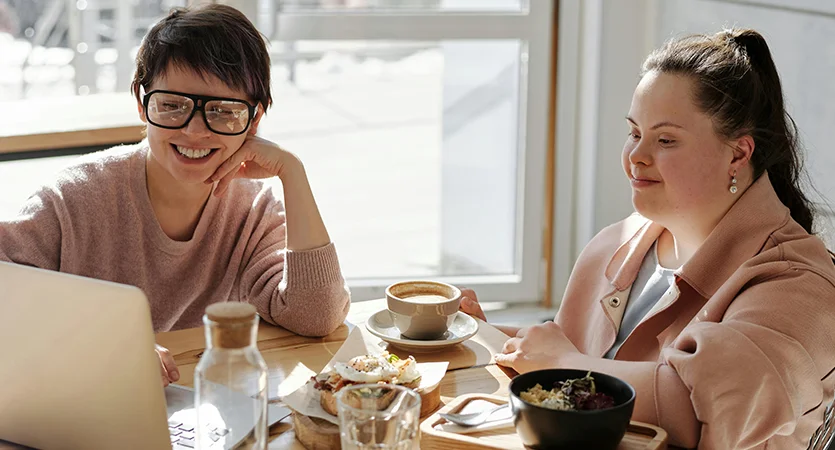 two people smiling at a cafe looking at a laptop