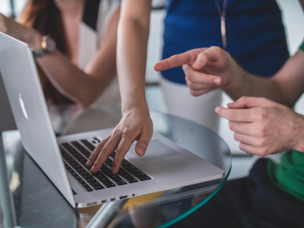 Group of people working around a laptop, with one pointing and explaining whats on the screen